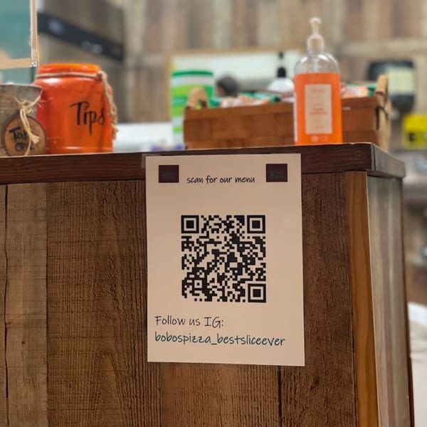 A QR code for Bobo's Pizza menu and Instagram, with a tip jar and hand sanitizer in the background.