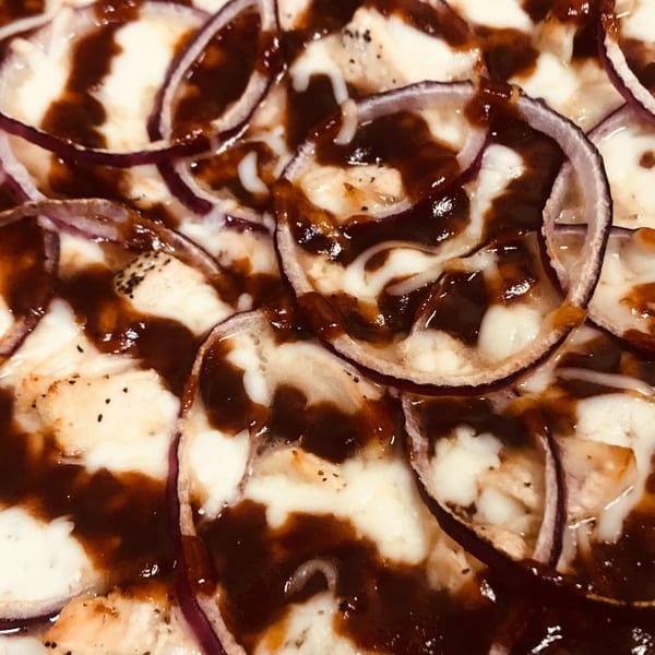 Close-up of Bobo's Pizza with red onions, melted cheese, and a dark sauce drizzle.