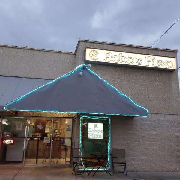 Bobo's Pizza storefront at dusk, with a lit sign and blue neon lights outlining the awning and door.