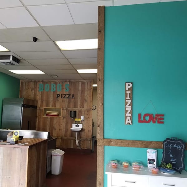 Interior of Bobo's Pizza with a wooden counter, teal walls, and "PIZZA LOVE" sign.