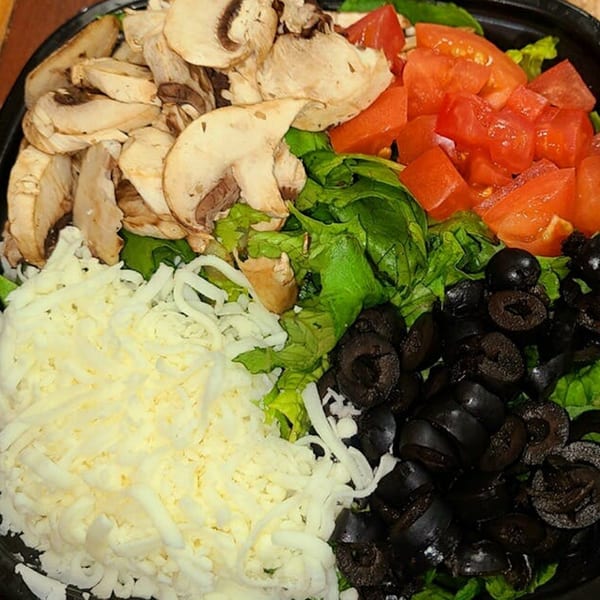 A salad with sliced mushrooms, diced tomatoes, shredded cheese, and black olives on a bed of lettuce.