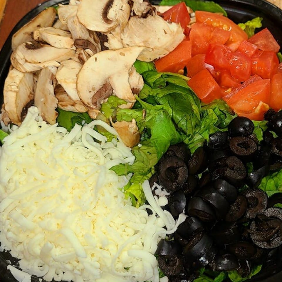 A salad with sliced mushrooms, diced tomatoes, shredded cheese, and black olives on a bed of lettuce.