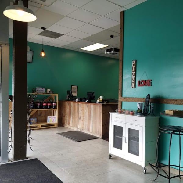 The interior of Bobo's Pizza features a wooden counter, teal walls, and "PIZZA LOVE" signage.