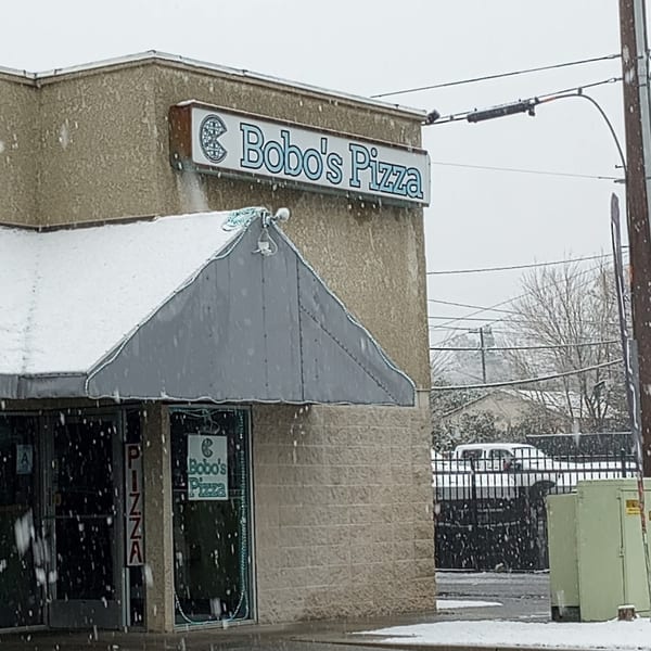 Bobo's Pizza restaurant exterior on a snowy day, with snow on the awning and ground.
