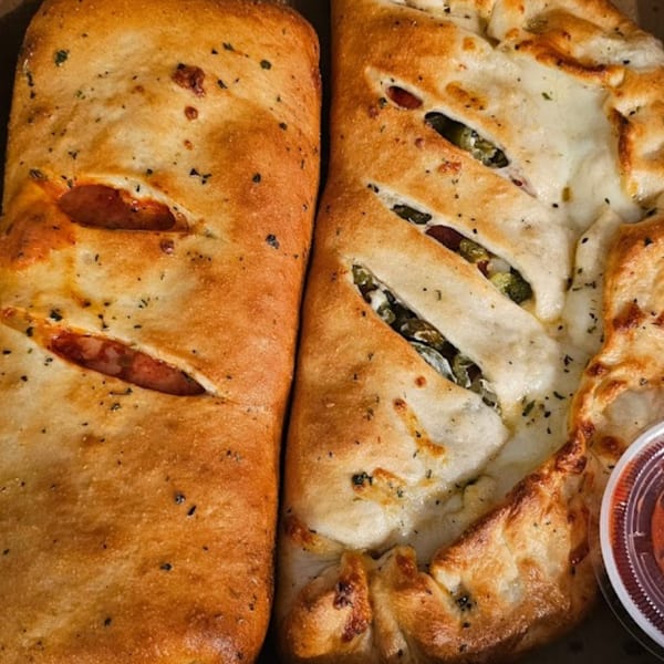 Two golden-brown Bobo's Pizza calzones, one with pepperoni and the other with visible fillings, and a side of sauce.
